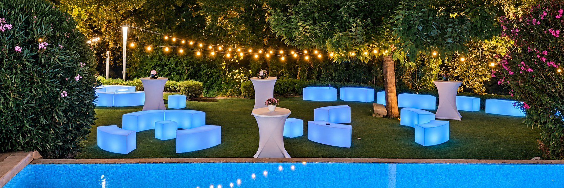 Bancs LED bleus et cubes dans un jardin sous des guirlandes au bord de la piscine