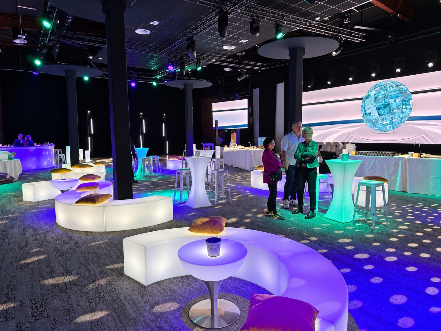 Bancs blancs formant des îlots lounge dans une salle éclairée en turquoise et violet