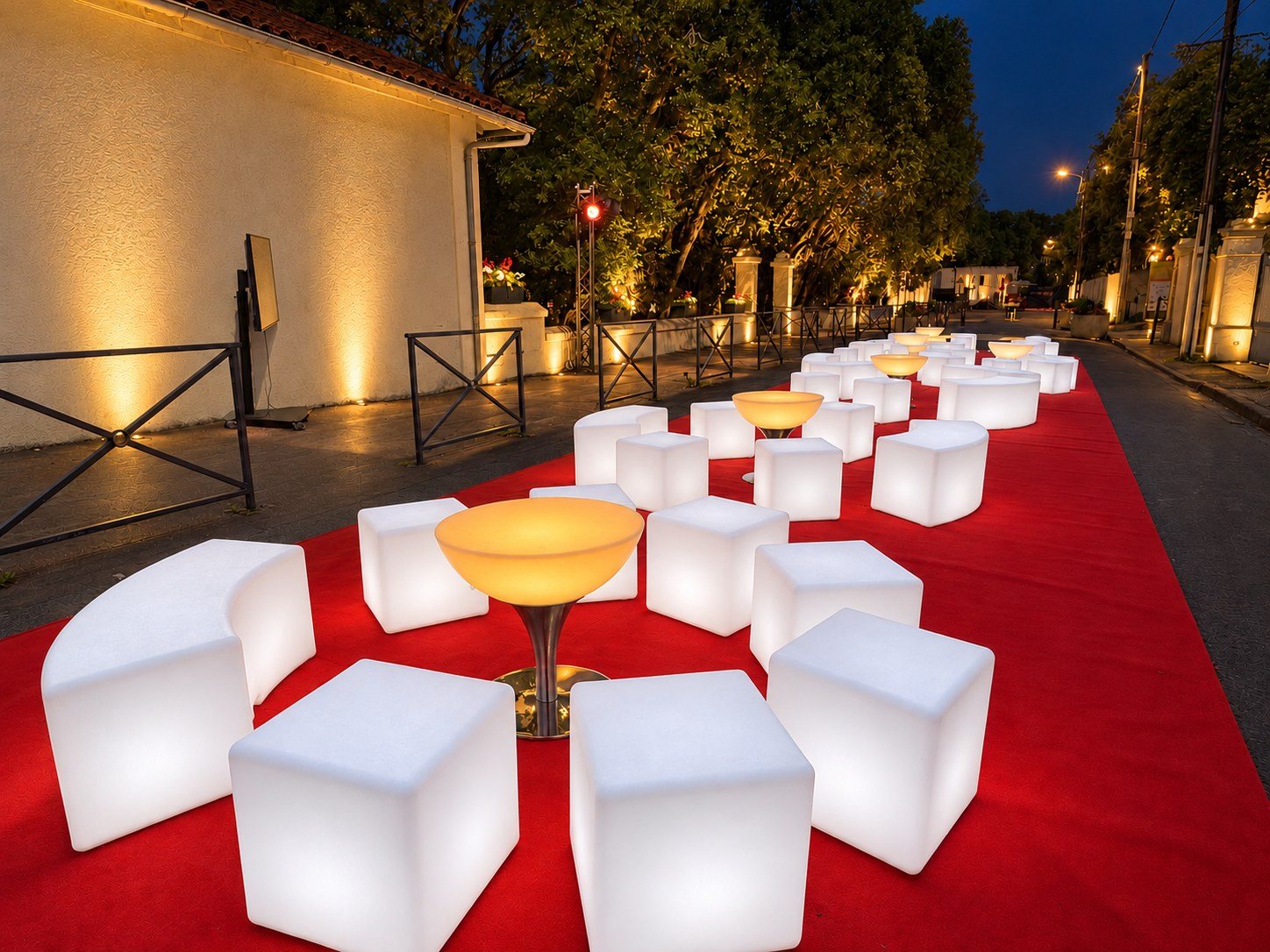 Enfilade de bancs arrondis blancs et cubes autour de tables ambrées sur tapis rouge