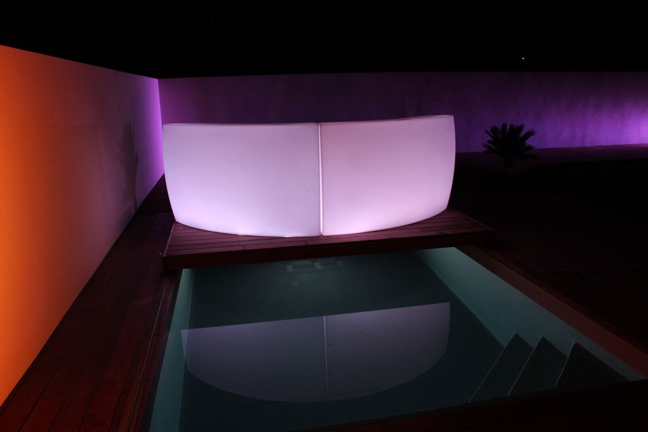 Bar lumineux arrondi violet dans une ambiance lounge près d’une piscine