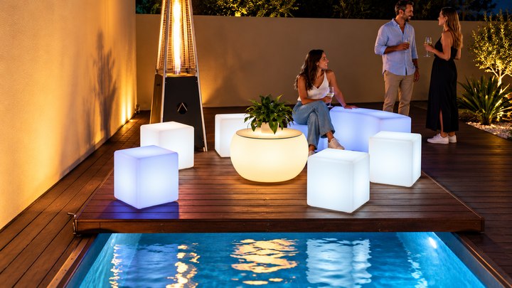 Cubes lumineux blancs et bleutés autour d’une table ambrée au bord de la piscine