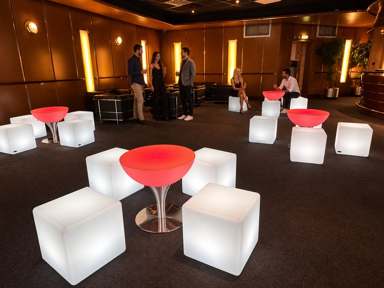 Tables Lounge rouges sur pied en inox, cubes blancs et invités dans un espace réception