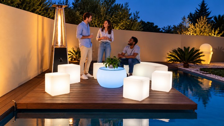 Table basse lumineuse bleue avec plateau en verre et cubes blancs au bord de la piscine