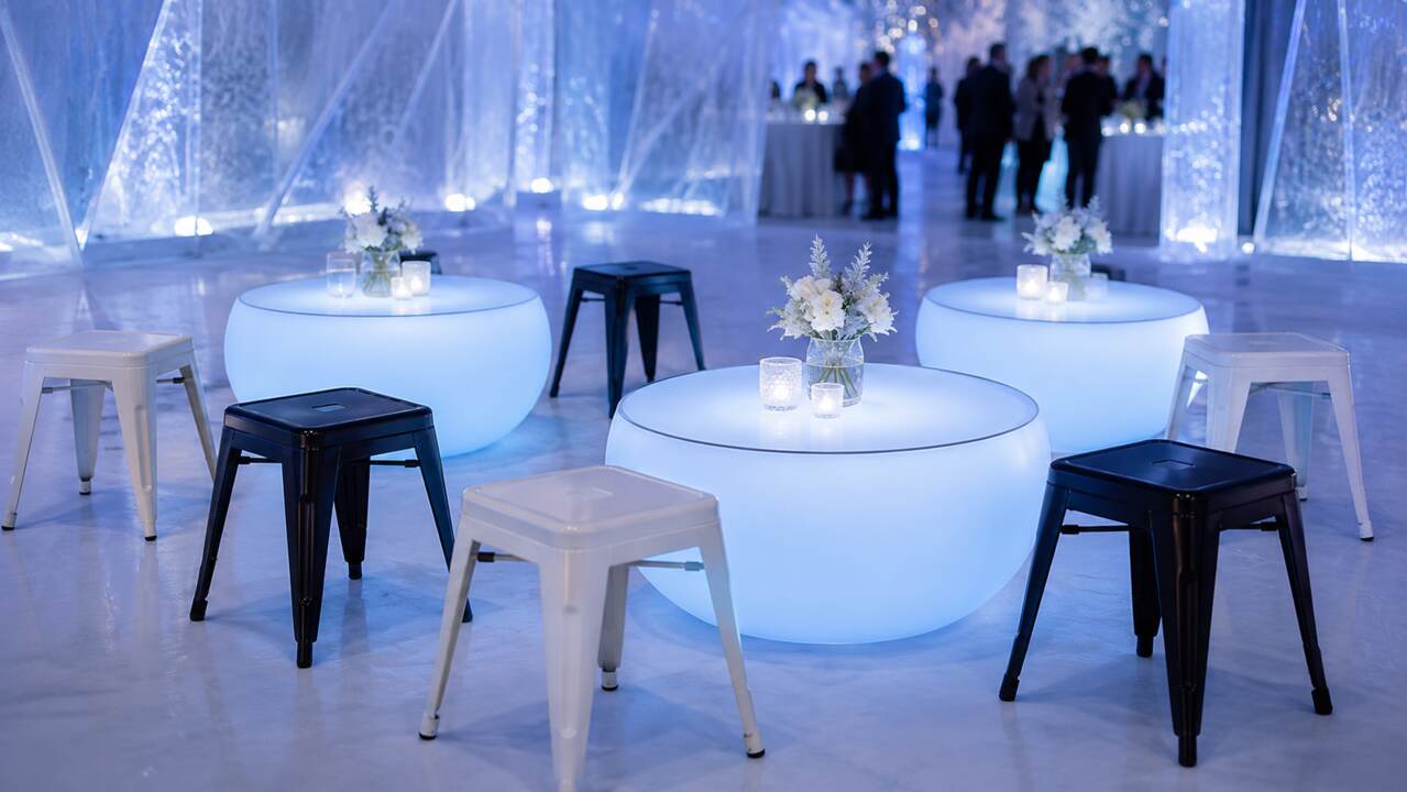 Tabourets bas acier noirs et blancs autour de tables lumineuses dans un décor glacé