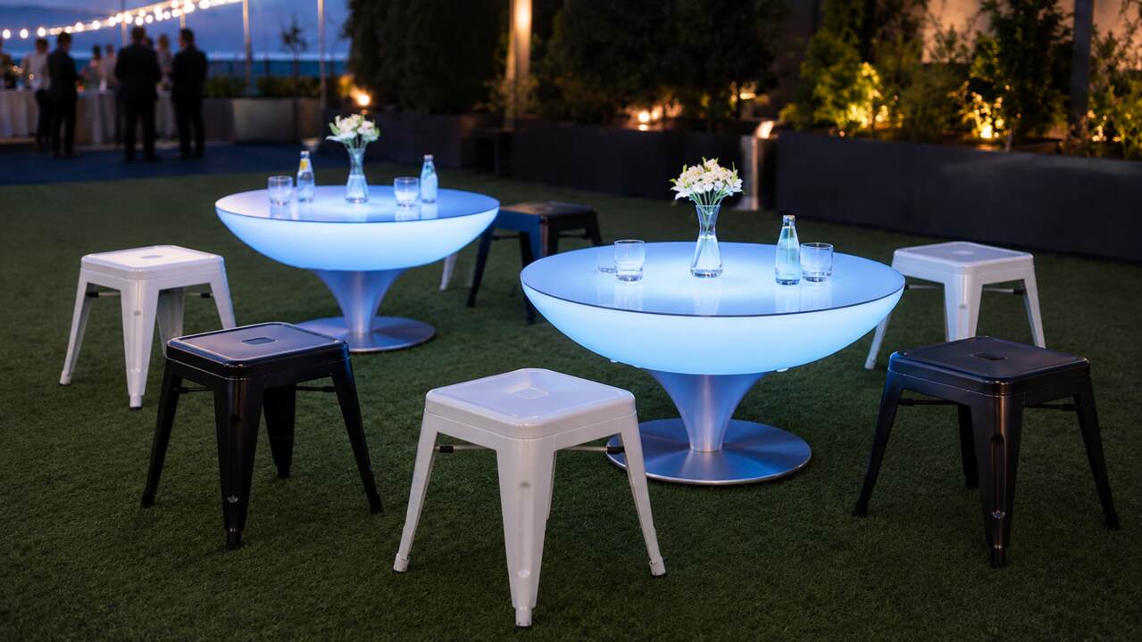 Tabourets bas acier noirs et blancs avec tables lumineuses sur une terrasse nocturne